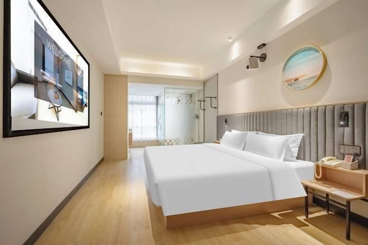 Una habitación de hotel moderna con una cama grande, un teléfono en la mesita de noche, un televisor montado en la pared y un cuadro enmarcado.