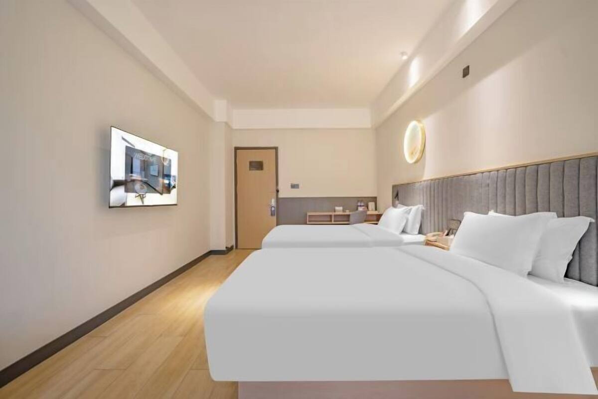 Una habitación de hotel con dos camas, una mesita de noche, un televisor montado en la pared y una puerta que da al baño.
