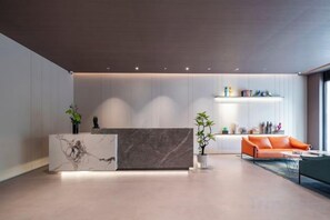Un espace d’accueil moderne avec un comptoir de réception en marbre, un canapé et une plante.