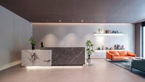 Un espace d’accueil moderne avec un comptoir de réception en marbre, un coin salon doté d’un canapé orange et une étagère ornée d’objets décoratifs.
