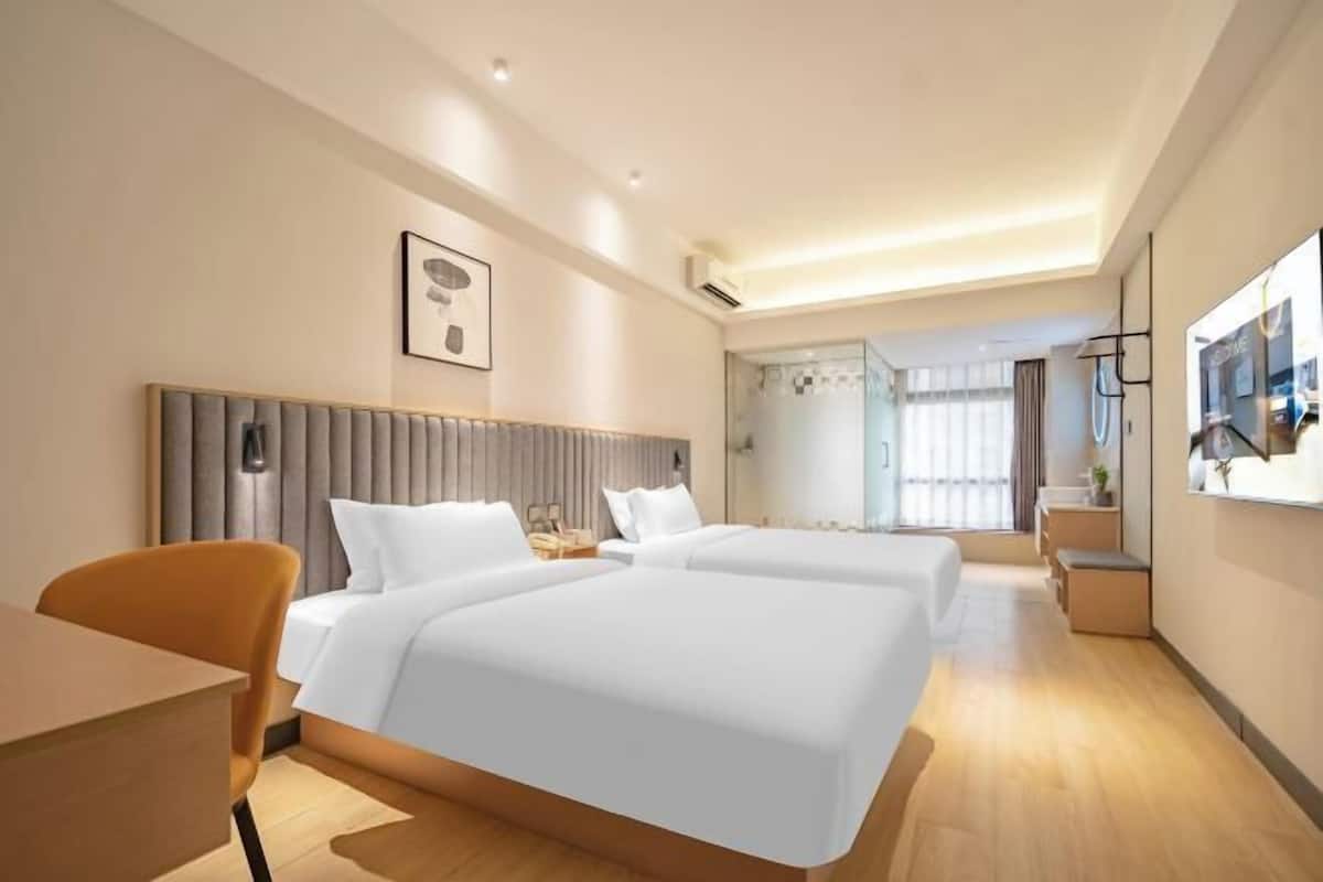 Una habitación de hotel con dos camas, un escritorio, una silla, una mesita de noche y un ventanal grande.