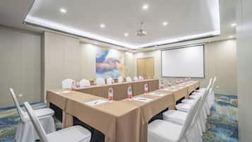 A conference room with a long table, white chairs, and a projector screen.