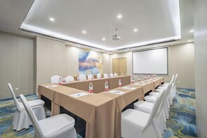 Une salle de conférence avec une longue table, des chaises blanches et un écran de projection.