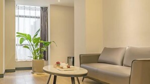 Un salon moderne avec un canapé, une table basse ronde, une plante en pot et une fenêtre avec des rideaux.