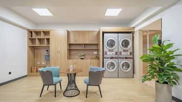 A compact living space with a dining area, built-in wooden shelving, a washing machine, and a potted plant.