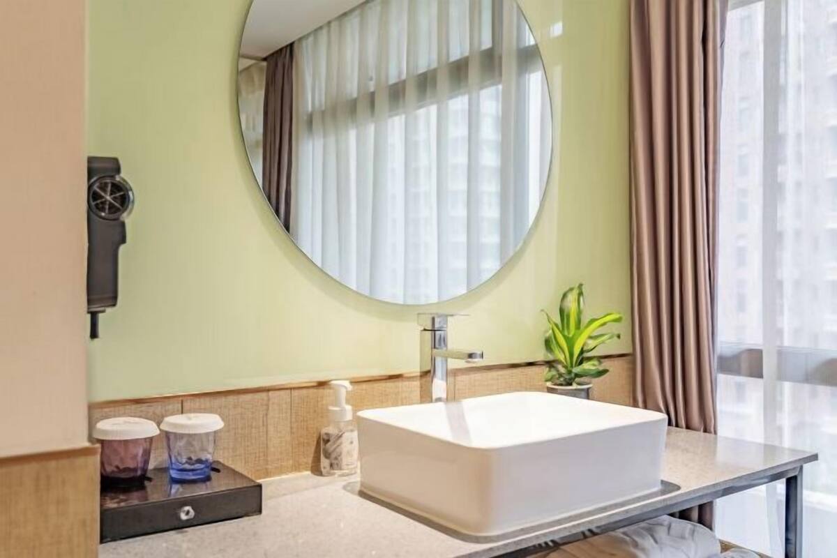 Un baño moderno con un espejo grande, un lavamanos blanco y una pequeña planta en la encimera.