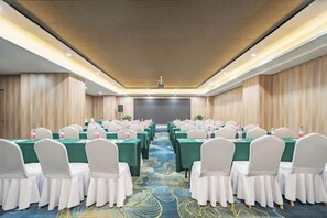 Une salle de conférence avec des rangées de tables et de chaises, un sol recouvert de moquette et un grand écran à l’avant.