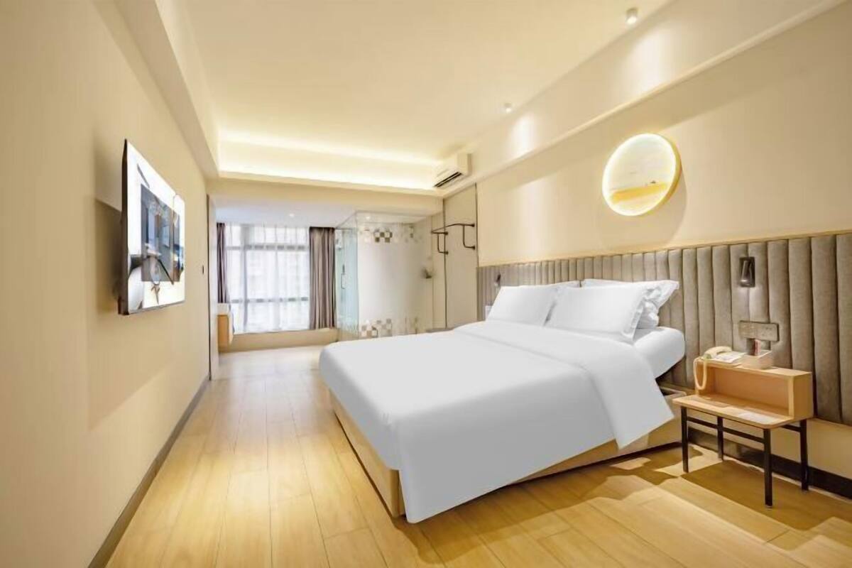 Una habitación de hotel moderna con una cama grande, una mesita de noche y vistas al pasillo.