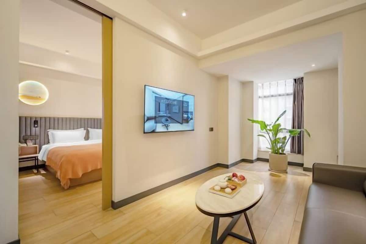 Una habitación de hotel moderna con cama, una mesita con aperitivos, un televisor de pared y una planta en maceta.