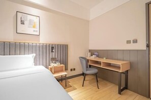 Ein Hotelzimmer mit einem Bett, einem Schreibtisch, einem Sessel und einem gerahmten Bild an der Wand.