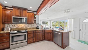 A kitchen with wooden cabinets, stainless steel appliances, and a large window offering a view of the outdoors. - Villa Paradisus. Heated Pool! 6 min to the beach (Satellite Beach)
