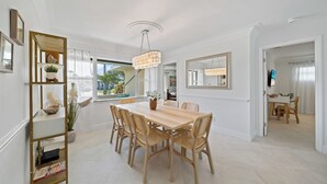 A dining area with a wooden table and wicker chairs, a chandelier, and a large mirror on the wall. - Villa Paradisus. Heated Pool! 6 min to the beach (Satellite Beach)