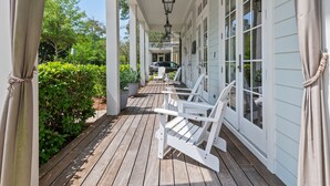Une terrasse en bois couverte, avec des chaises blanches, et une voiture garée à l’arrière-plan.