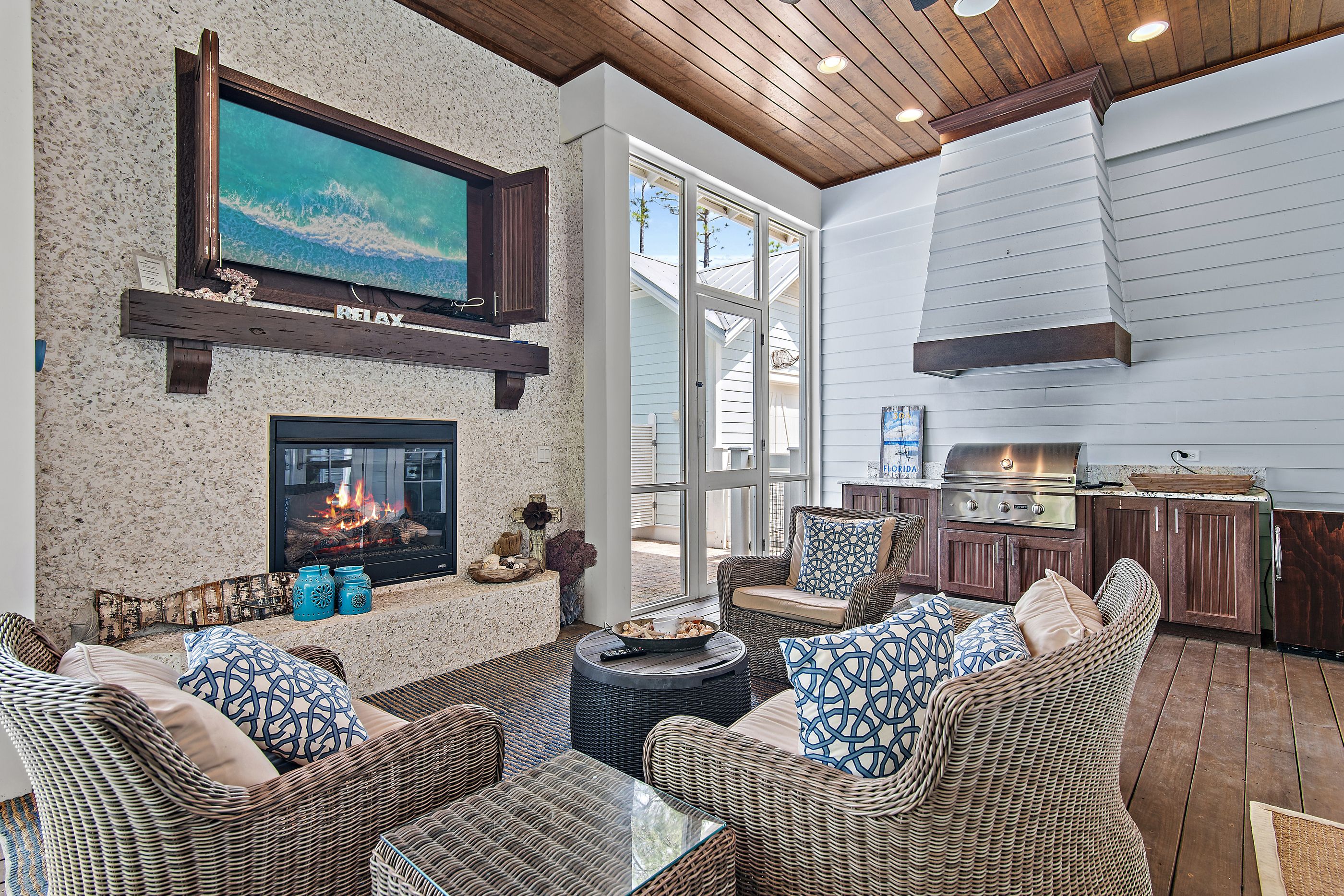 A cozy outdoor living area with wicker furniture, a fireplace, and a TV mounted on a stone wall.