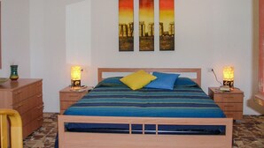 A bedroom with a bed, two bedside tables, a nightstand, a wooden dresser, and a wall-mounted painting. - Villa da Anna e Turi - 5 minutes from the beach (San Gavino ( frazione di Budoni))
