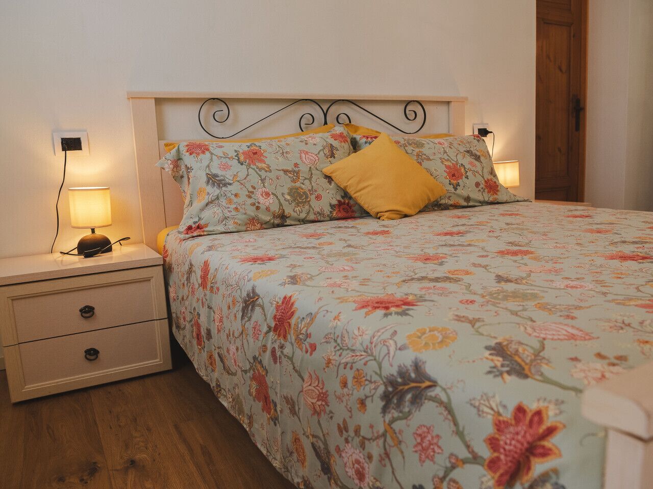 A bedroom with a floral bedspread, two bedside tables with lamps, and a wooden door.