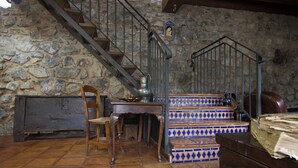 Ein rustikaler Raum mit Steinwand, Holztisch, Stuhl, Bank und einer Treppe mit blauen und weißen Fliesen.
