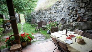 Eine Terrasse im Freien mit einer Steinsäule, Holzstühlen, einem für eine Mahlzeit gedeckten Tisch und Blumentöpfen.