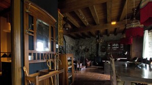 Ein rustikales Interieur mit Holzbalken, einer Steinwand und einem Essbereich mit Tisch und Stühlen.
