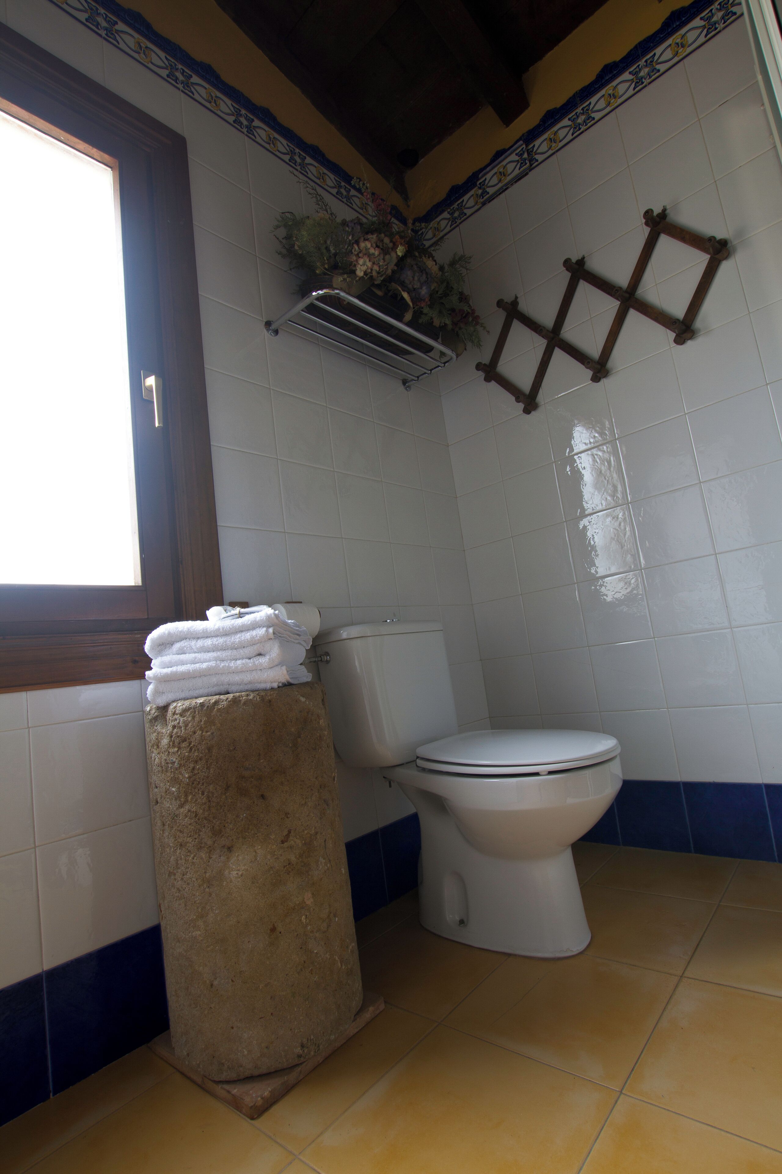A bathroom with a toilet, a towel stack, and a window.