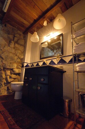 Une salle de bain avec un mur en pierre, un plafond en bois, un lavabo avec un miroir et un porte-serviettes.