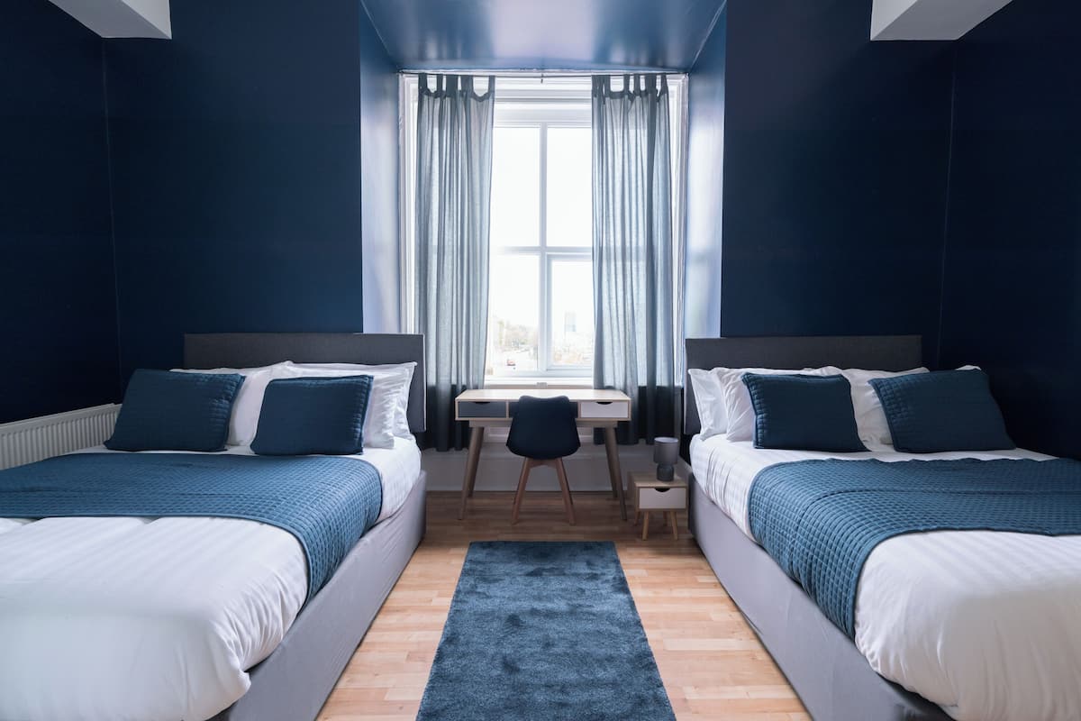 Une chambre avec deux lits, un bureau et une fenêtre avec des rideaux.