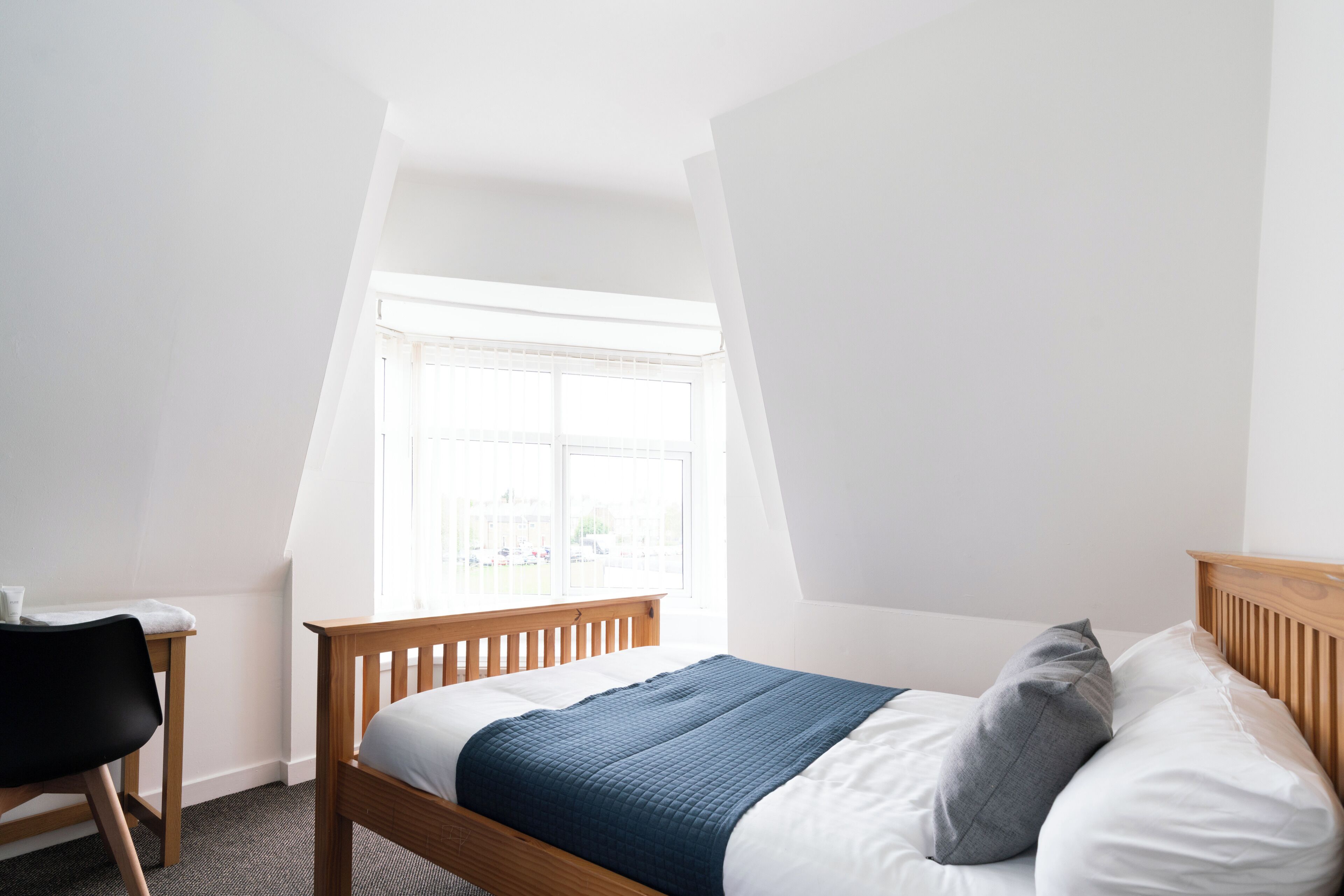 Een slaapkamer met een houten bed, een bureau en een raam met jaloezieën.
