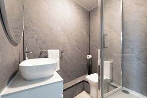 Een moderne badkamer met een groot wit wastafel, toilet en een douchecabine met glazen wanden.