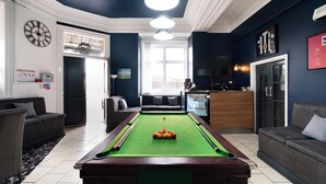 A pool table in a room with a dark blue wall, a clock, and a television. - Citysteps Hotels Newcastle West (Newcastle-upon-Tyne)