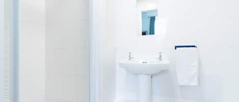 A modern bathroom with white tiles, a pedestal sink, a mirror, and a shower enclosure.