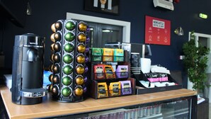 A coffee station with a coffee machine, a display of coffee pods, and a sign for Newcastle Hotel & Bar. - Citysteps Hotels Newcastle West (Newcastle-upon-Tyne)