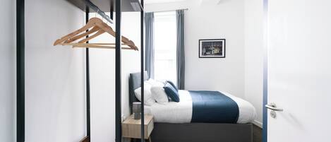A modern hotel room with a bed, bedside table, and a wardrobe with a wooden hanger.