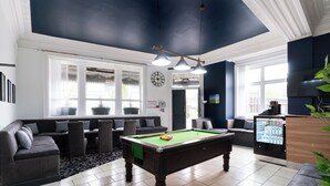 A billiards table in a room with a dark ceiling, a clock on the wall, and a refrigerator with beverages. - Citysteps Hotels Newcastle West (Newcastle-upon-Tyne)