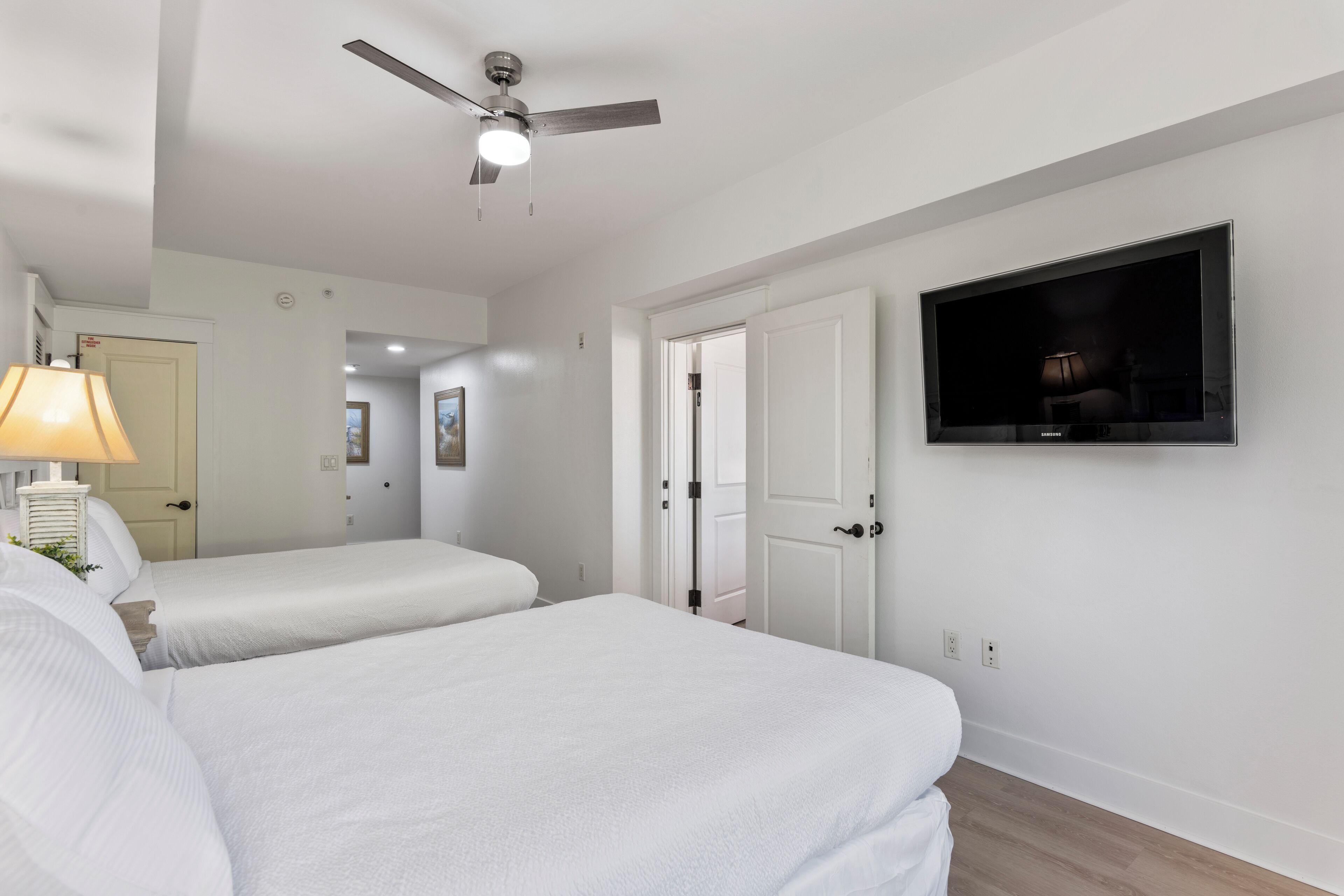 A hotel room with two beds, a ceiling fan, a TV, and a lamp.