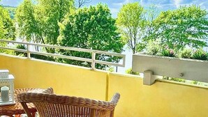 Een balkon met rieten meubilair, een leuning en uitzicht op bomen.