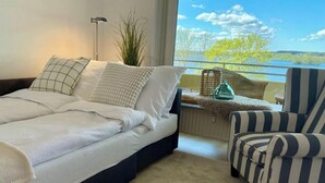 Een slaapkamer met een bed, een stoel, een lamp en uitzicht op een meer.