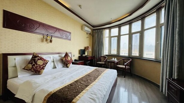 A hotel room with a large bed, a desk, a chair, and a view of the city through large windows. - Kuqa Haodu Business Hotel (Kuqa)