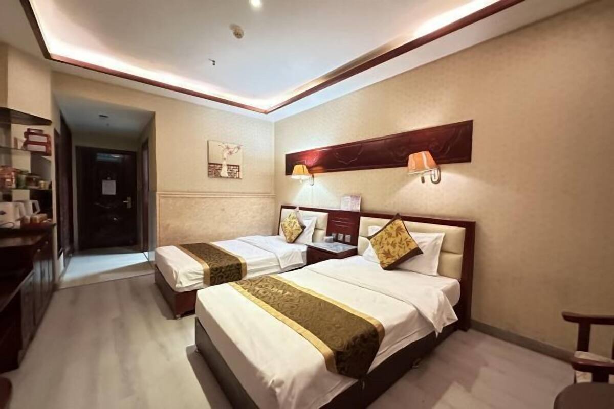 A hotel room with two beds, a desk, a chair, a lamp, and a painting on the wall.