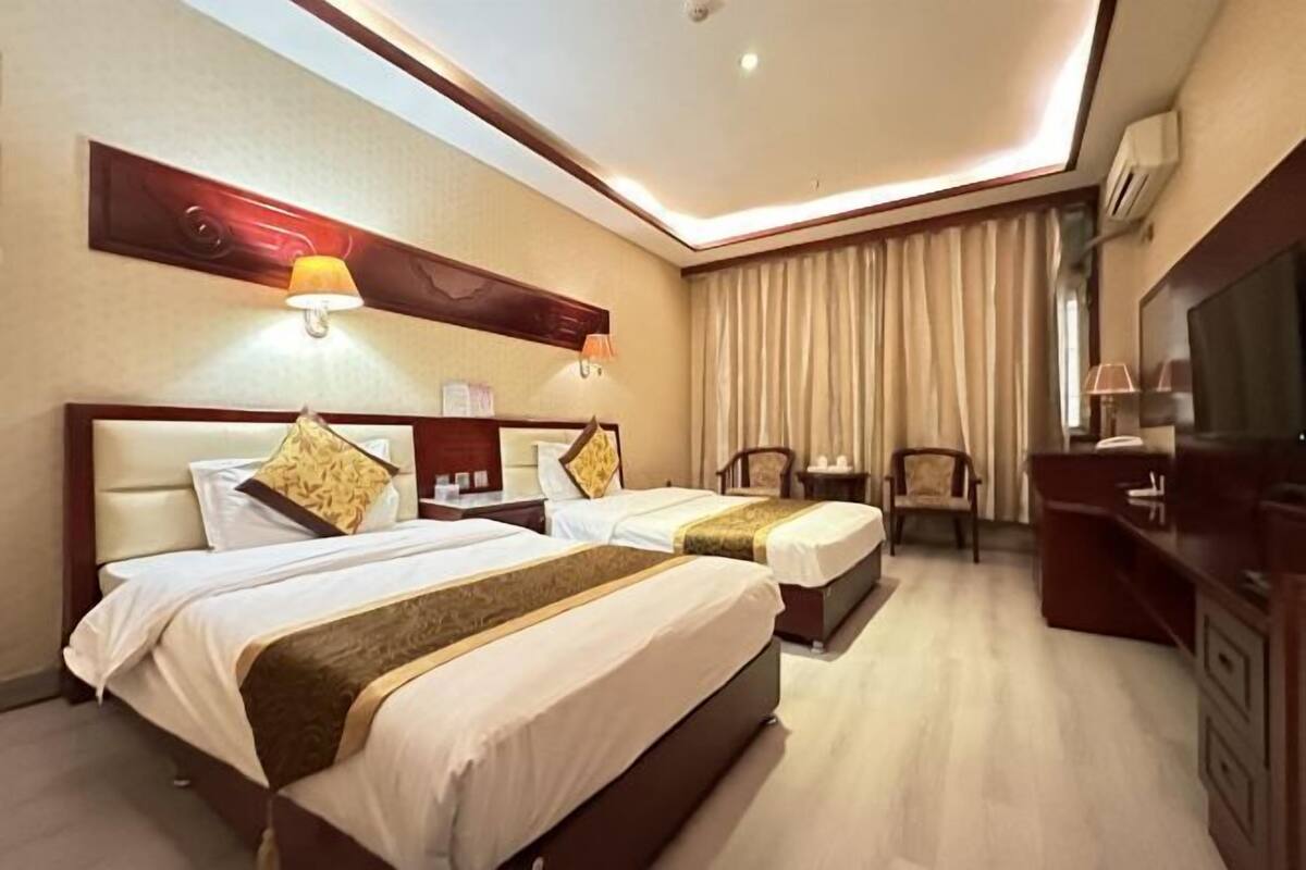 A hotel room with two beds, a desk, a chair, and a television.