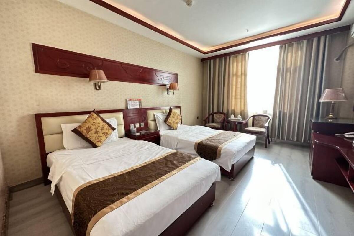 A hotel room with two beds, a desk, a chair, a lamp, and a window with curtains.