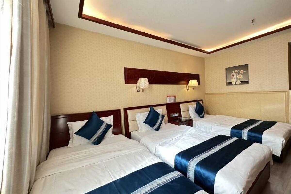 A hotel room with three beds, a nightstand, a wall-mounted lamp, and a framed picture.