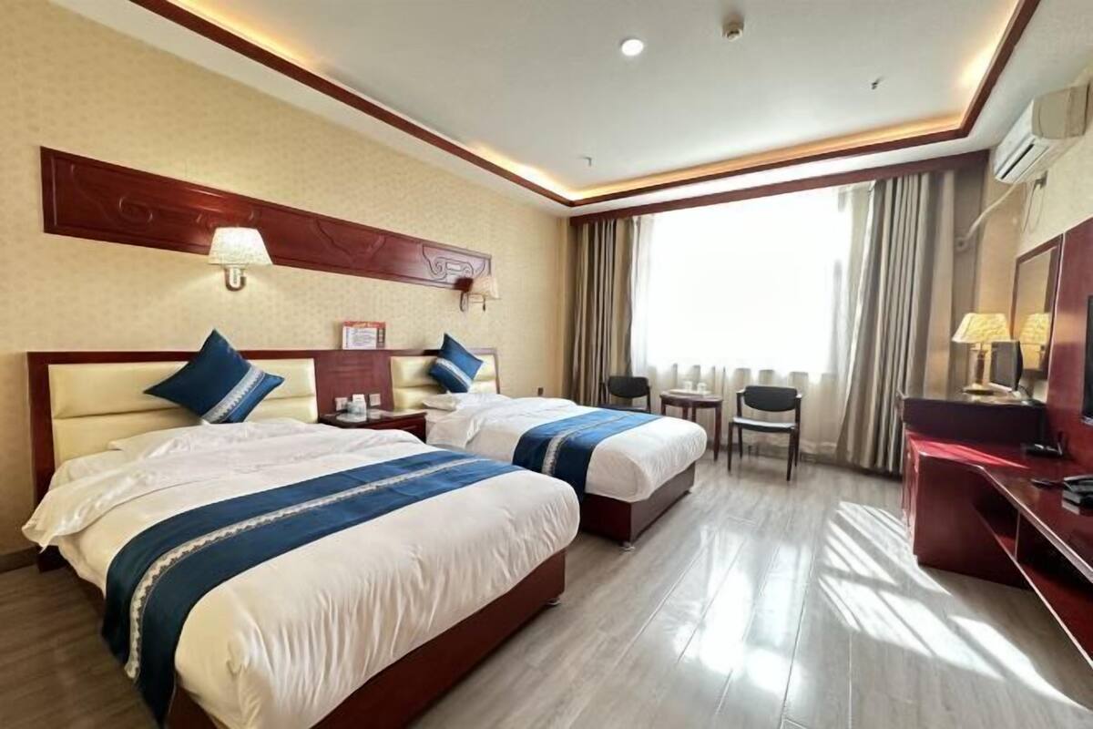 A hotel room with two beds, a desk, a chair, a TV, and a window with curtains.