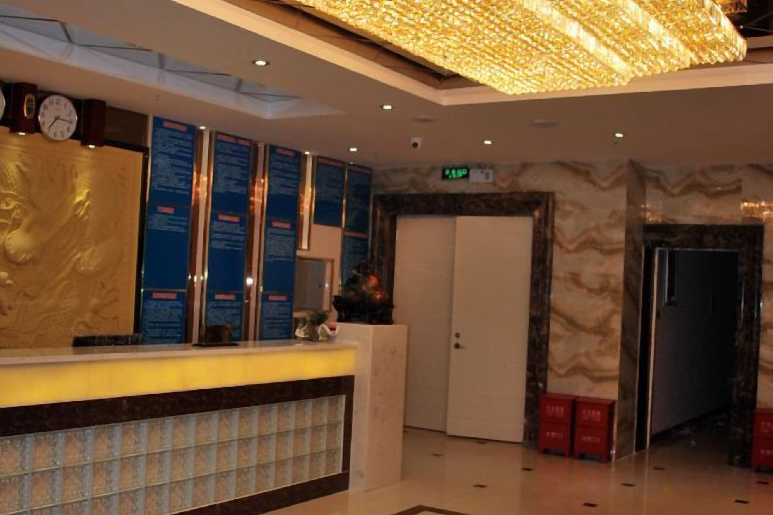 Zona de recepción de hotel con mostrador, paneles informativos, un reloj y una puerta.