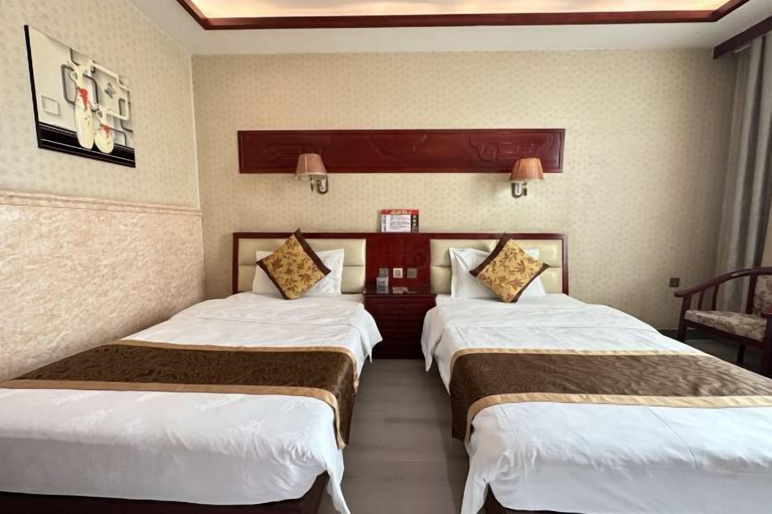 Habitación de hotel con dos camas, cabecero de madera, lámpara de pared y una pequeña mesa con una tarjeta.