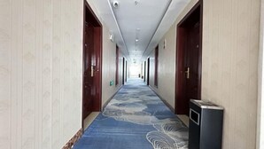 A hotel corridor with patterned wallpaper, a blue carpet with floral designs, and wooden doors. - Kuqa Haodu Business Hotel (Kuqa)