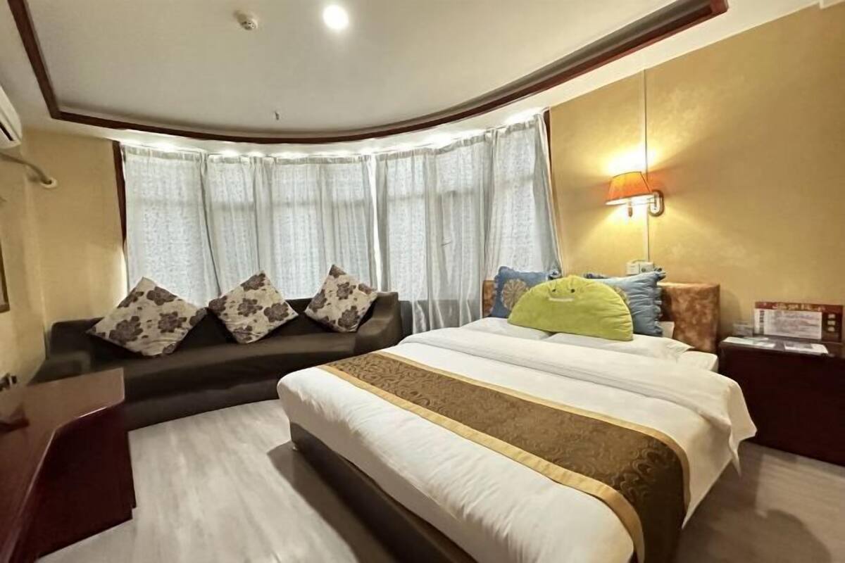 A hotel room with a large bed, a sofa, a desk, and a lamp.