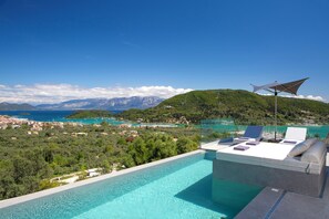 A rooftop infinity pool with a view of a coastal town and mountains. - Pothos Villas (Lefkada)