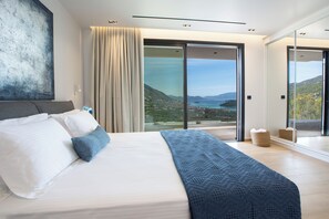 A modern bedroom with a large bed, a view of the outdoors, and a sliding glass door. - Pothos Villas (Lefkada)