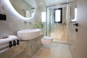A modern bathroom with a large white sink, a glass shower enclosure, and a marble wall. - Pothos Villas (Lefkada)
