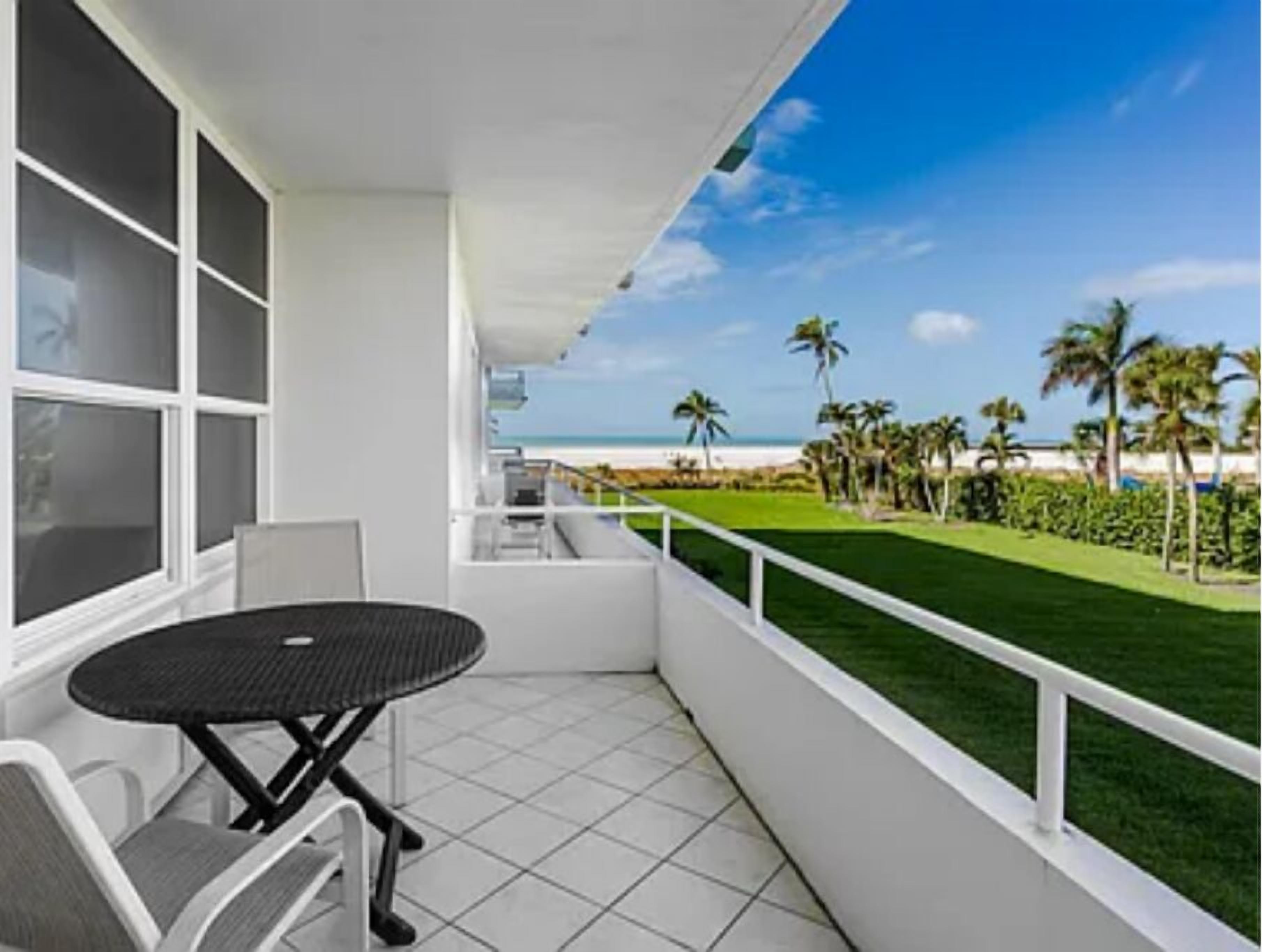 A balcony with a view of the beach, a table, and chairs.